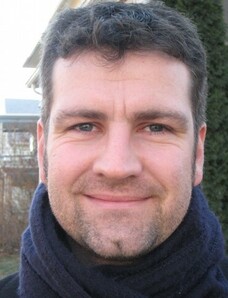 Herr Rachel mit dunkler Jacke und Schal, draußen im Porträt.